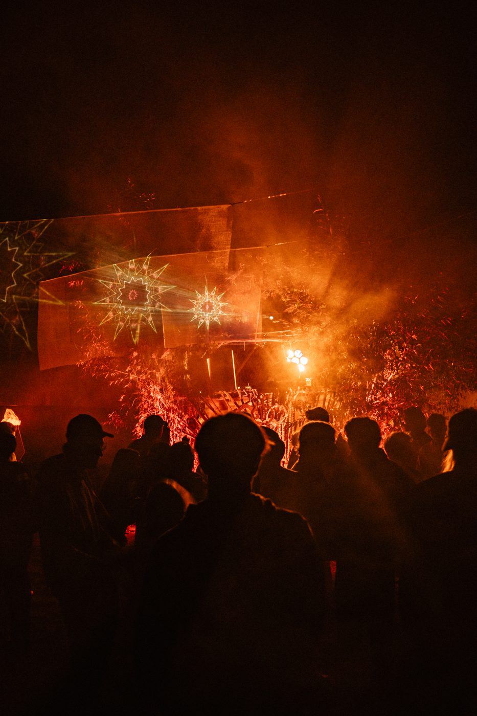Crowd at night in front of a stage with red light and laser projections