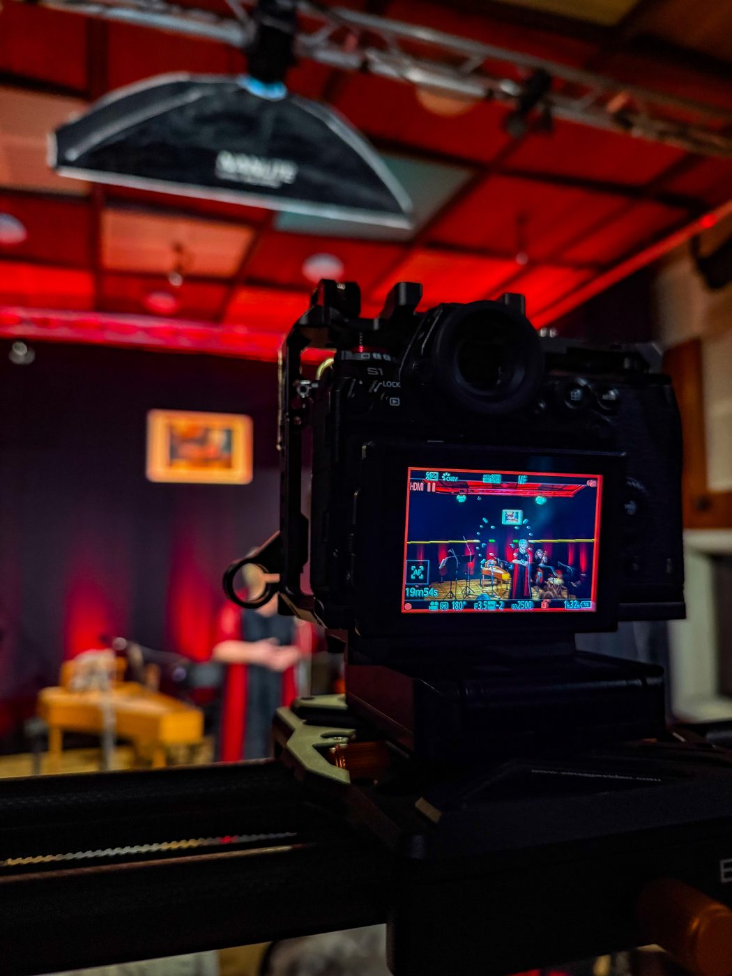 Camera monitor framing a concert on a red-lit stage