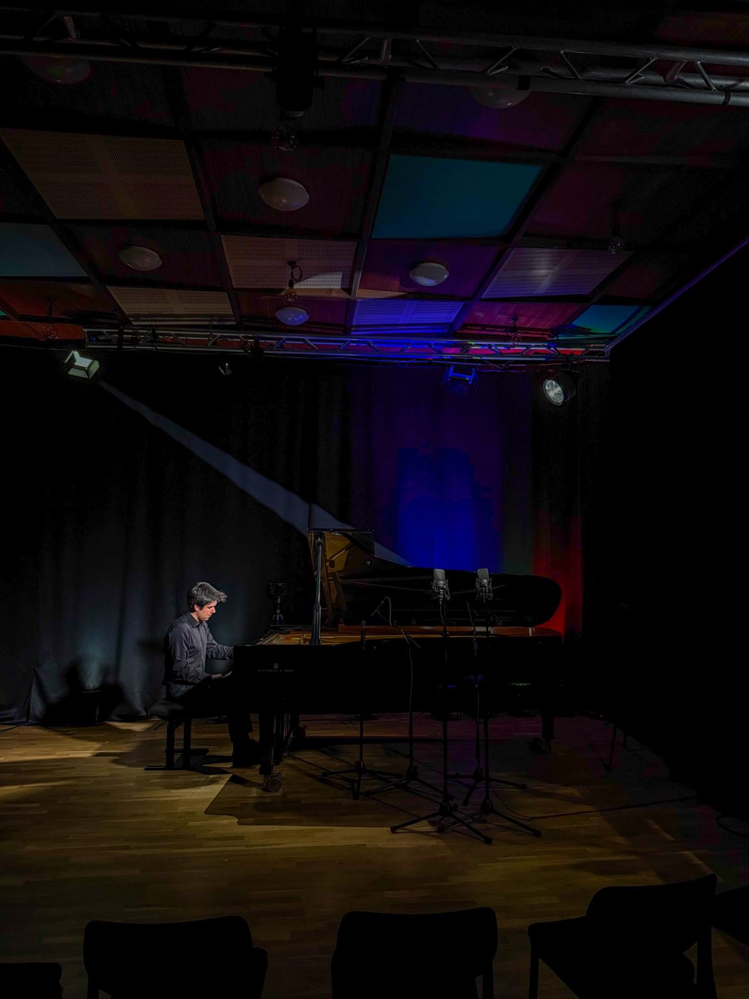 Pianist alone on a dark stage lit in blue and red