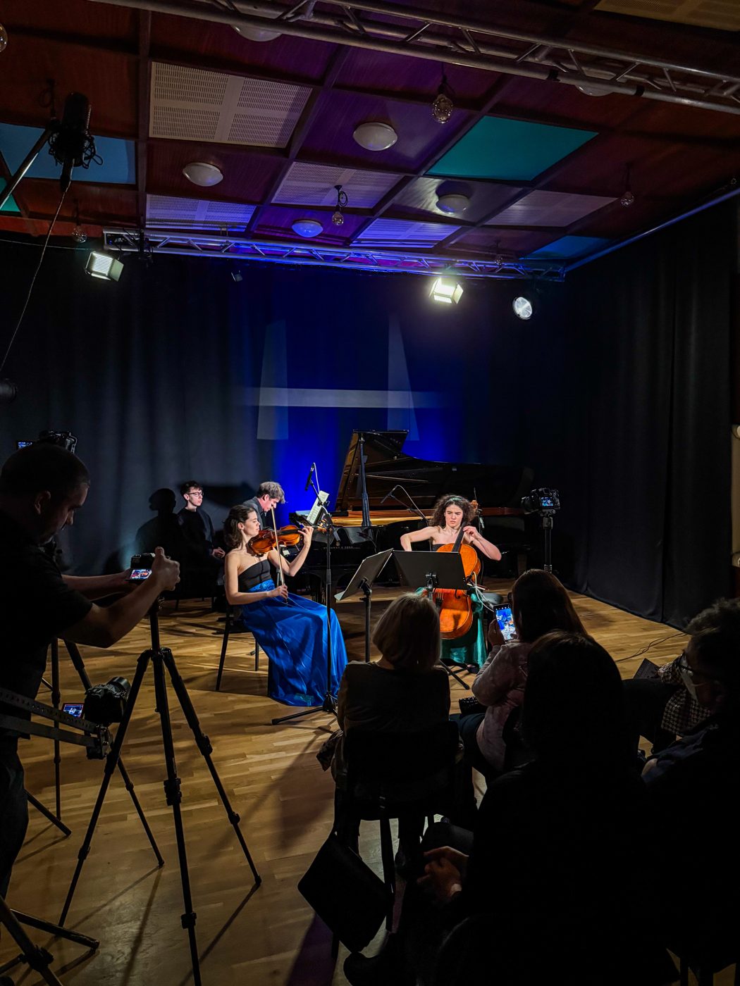 Piano trio performing for an audience while a camera operator films