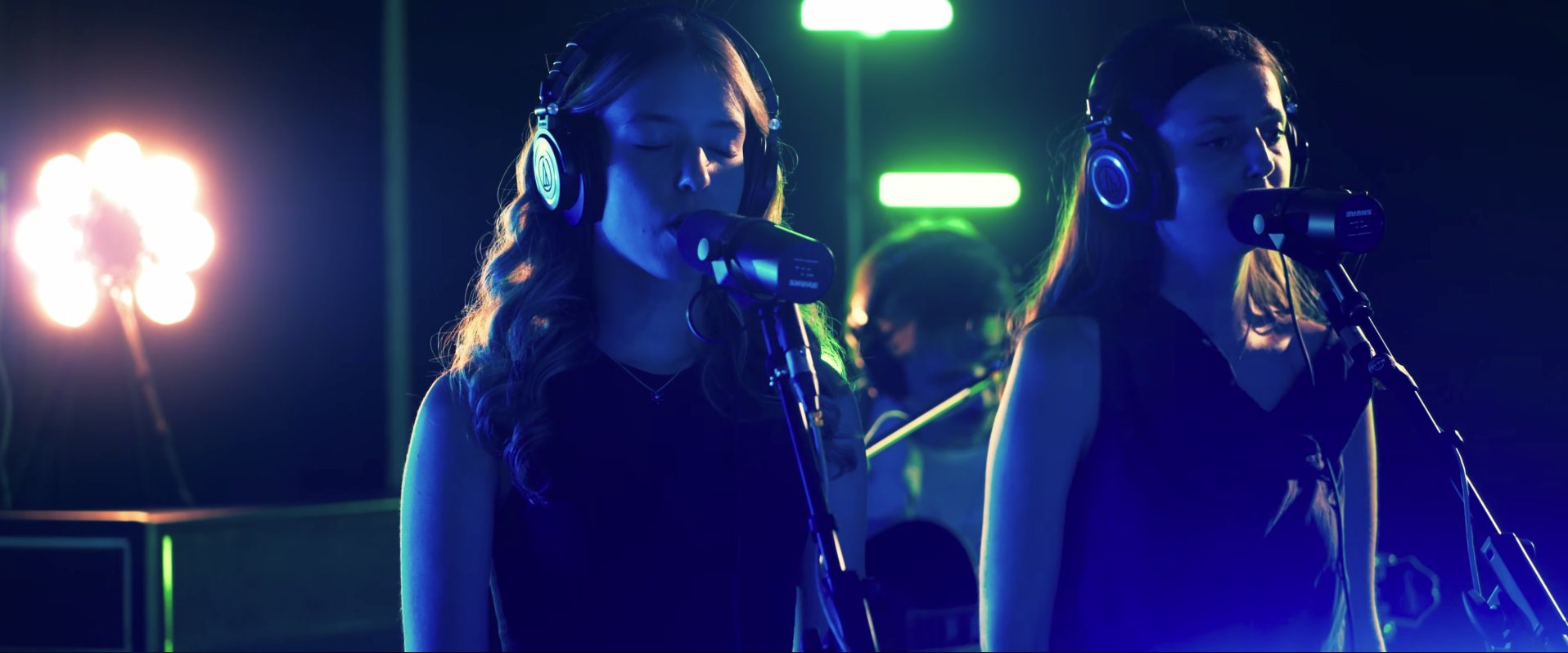 Two singers with headphones under blue and green light